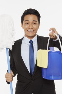 Businessman holding up a mop and other cleaning supplies